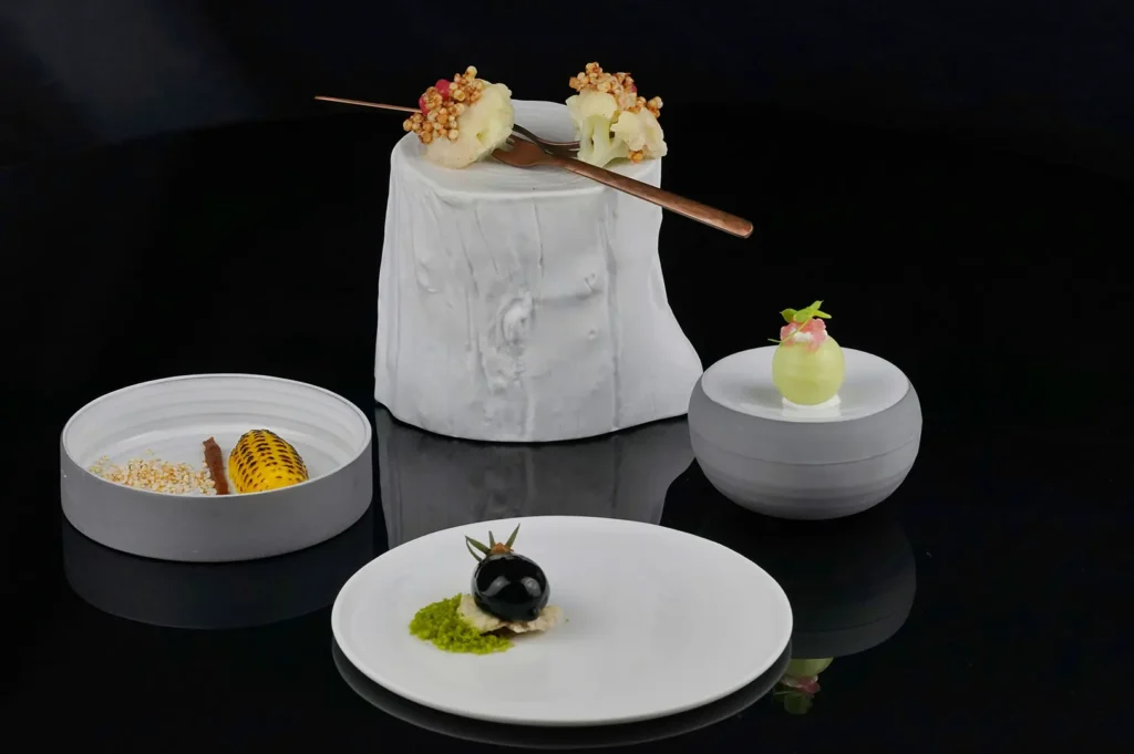 Fine dining food photography featuring dramatic low-key lighting and sharp specular highlights on minimalist plated dishes against a black background.