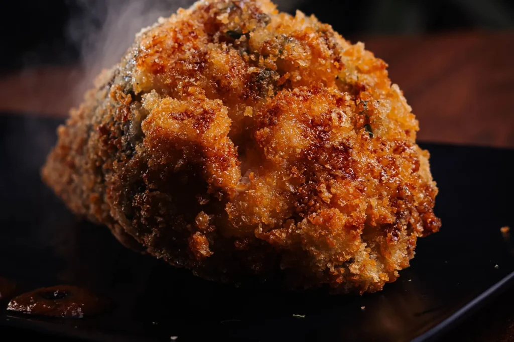 Crispy golden-brown breaded baked cauliflower head on a black plate.