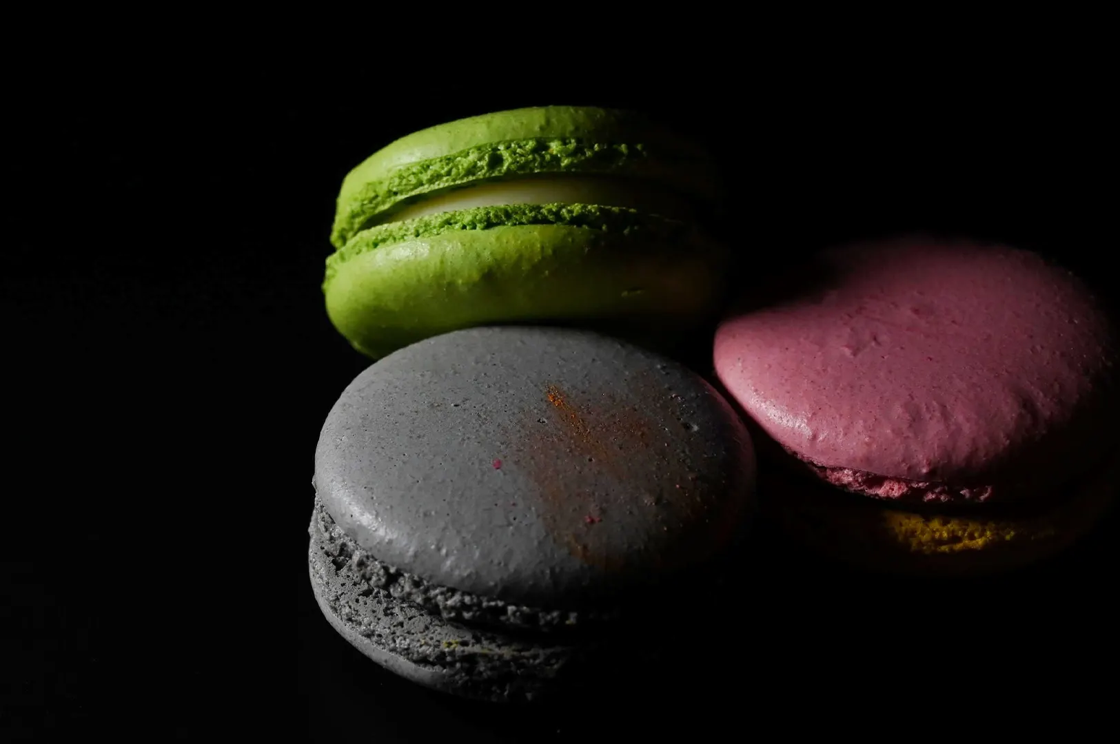 Dark moody food photography of colorful macarons on a black background representing RAW image files.