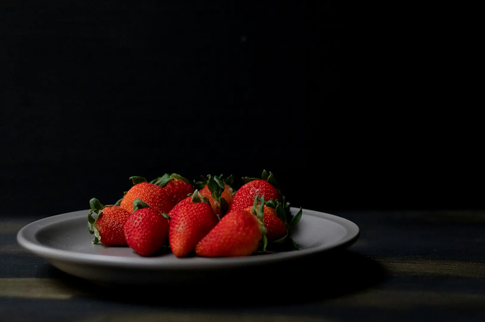 Dark, moody food photography of fresh red strawberries on a gray plate against a black background.