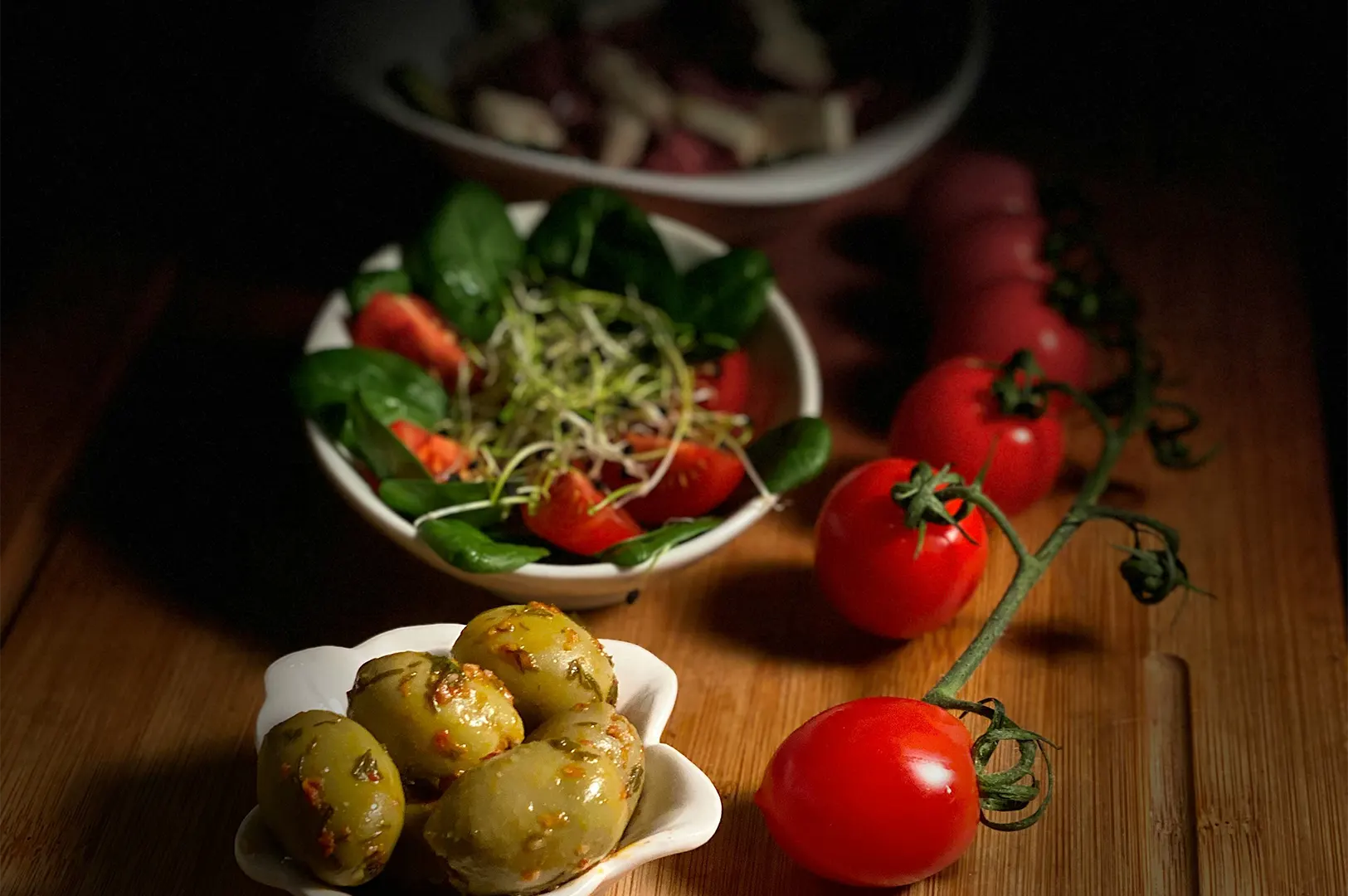 Moody dark food photography setup featuring fresh salad, olives, and tomatoes for buffet styling.