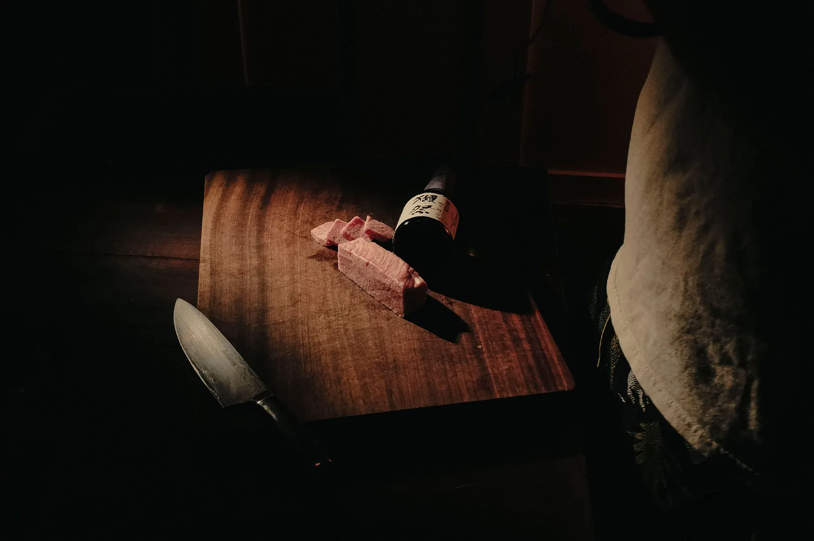 Dark moody food photography showcasing sliced wagyu beef on a wooden cutting board with a chef knife.