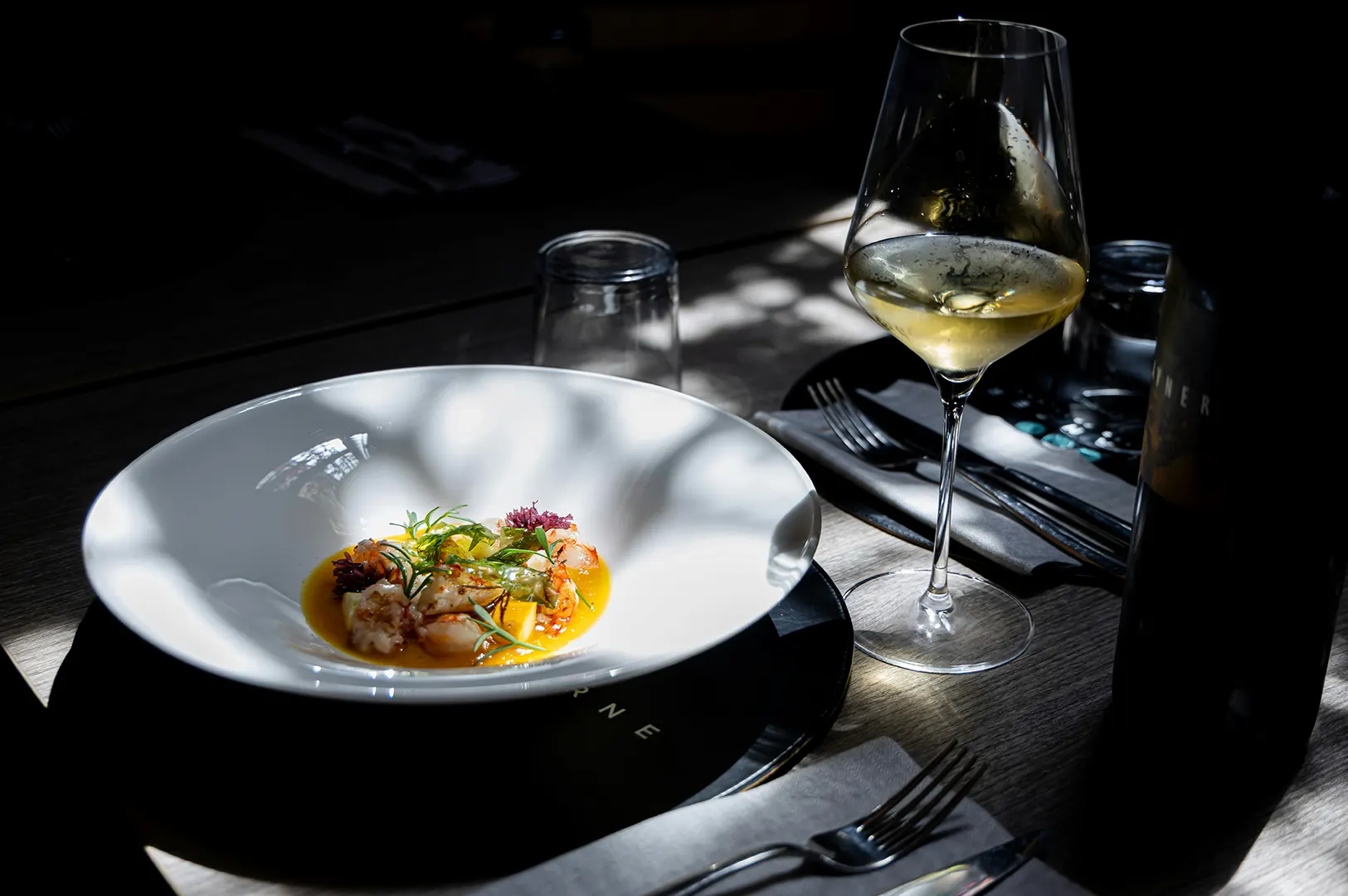 Moody dark food photography of a luxury plated dish and wine glass for restaurant marketing and PR pitch.