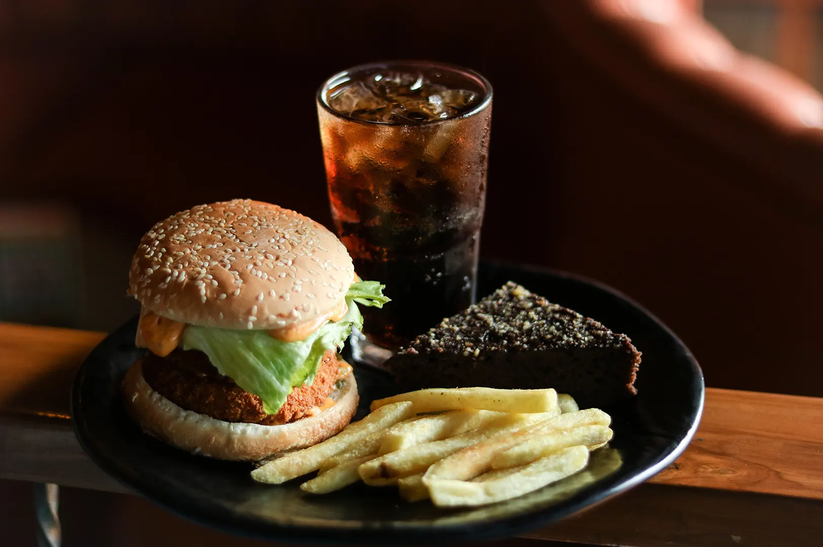 A complete set meal with a burger, fries, drink, and dessert served on a black plate.