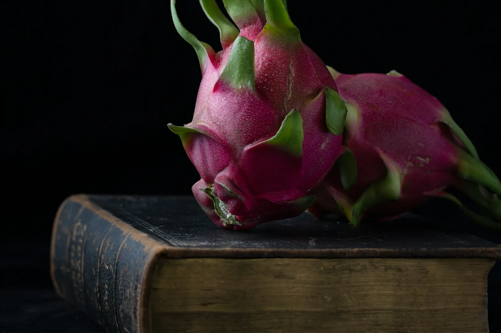 Moody dark food photography of dragon fruit resting on an old heritage book against a black background.