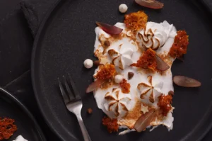 Gourmet deconstructed dessert with toasted meringue, honeycomb brittle, and sliced grapes on a dark plate.