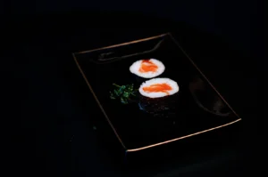 Two pieces of salmon maki sushi rolls served on a black plate with garnish.