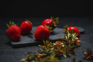 Close-up of fresh red strawberries on black stone, featuring atmospheric lighting and soft glare.