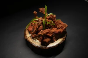 Crispy fried chicken pieces garnished with green onions served in a rustic wooden bowl.