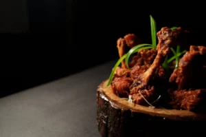 Crispy chicken lollipop served on a rustic wooden board with green garnish.