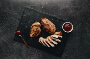 Grilled chicken breast served on a dark slate board with dipping sauce.