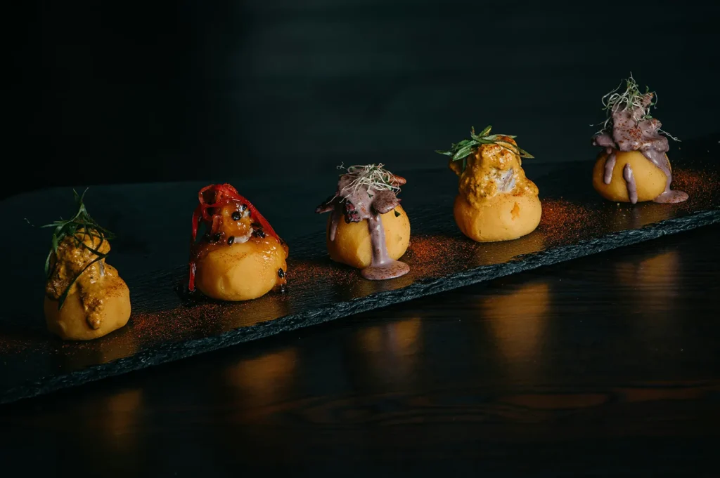 Dark moody food photography of gourmet potato dishes served on a black slate plate.