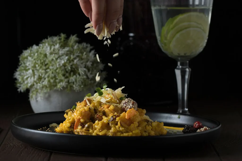 Dark food photography of a chef sprinkling cheese over a dish in a restaurant setting.