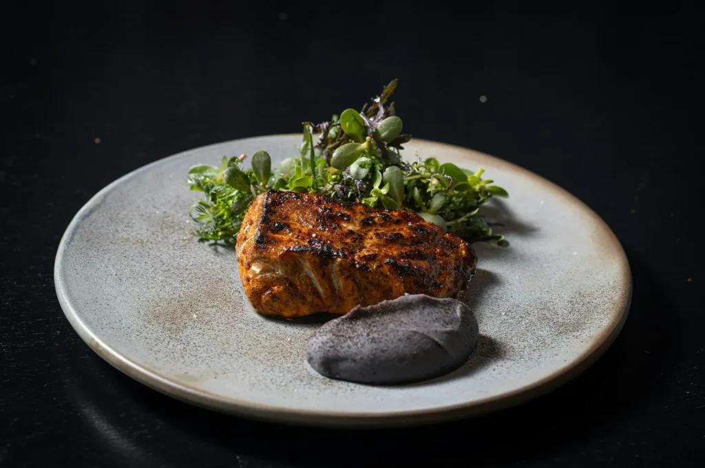 Close-up of gourmet seared fish with herbs and paste on a plate for food photography editing demonstration.