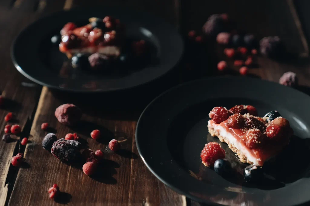 Dark moody food photography of berry cheesecake slices served on black plates for a buffet dessert station.