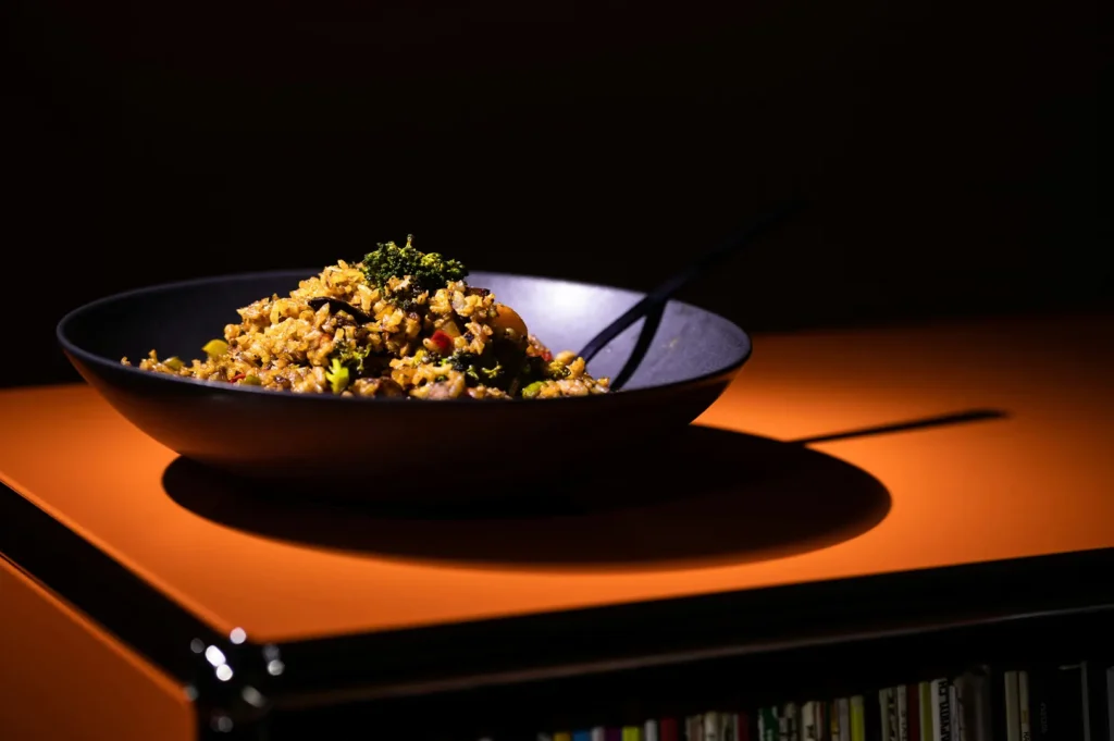 Dark moody food photography of a rice dish in a black bowl on an orange surface.