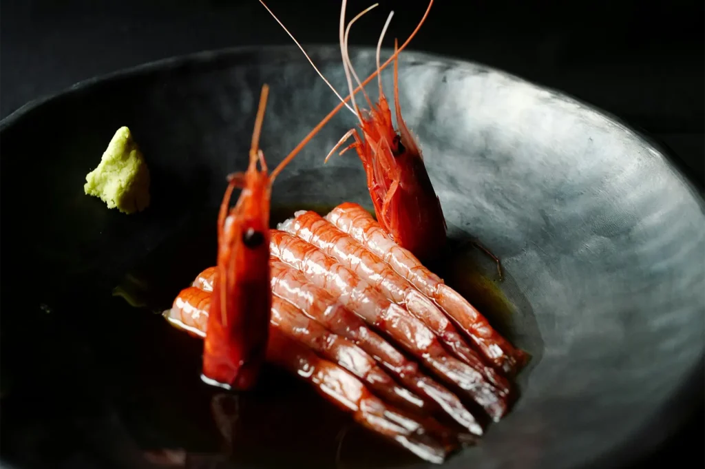 Dark moody food photography of fresh shrimp sashimi served on a black plate with wasabi.