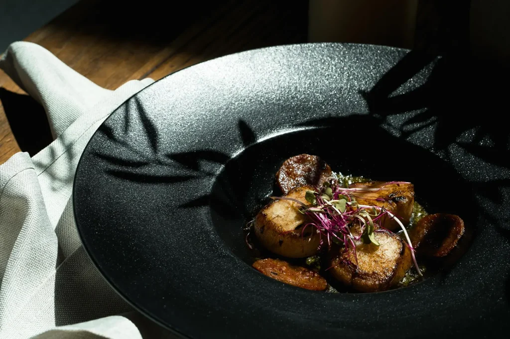 Dark food photography of seared scallops on a black plate with dramatic side lighting.