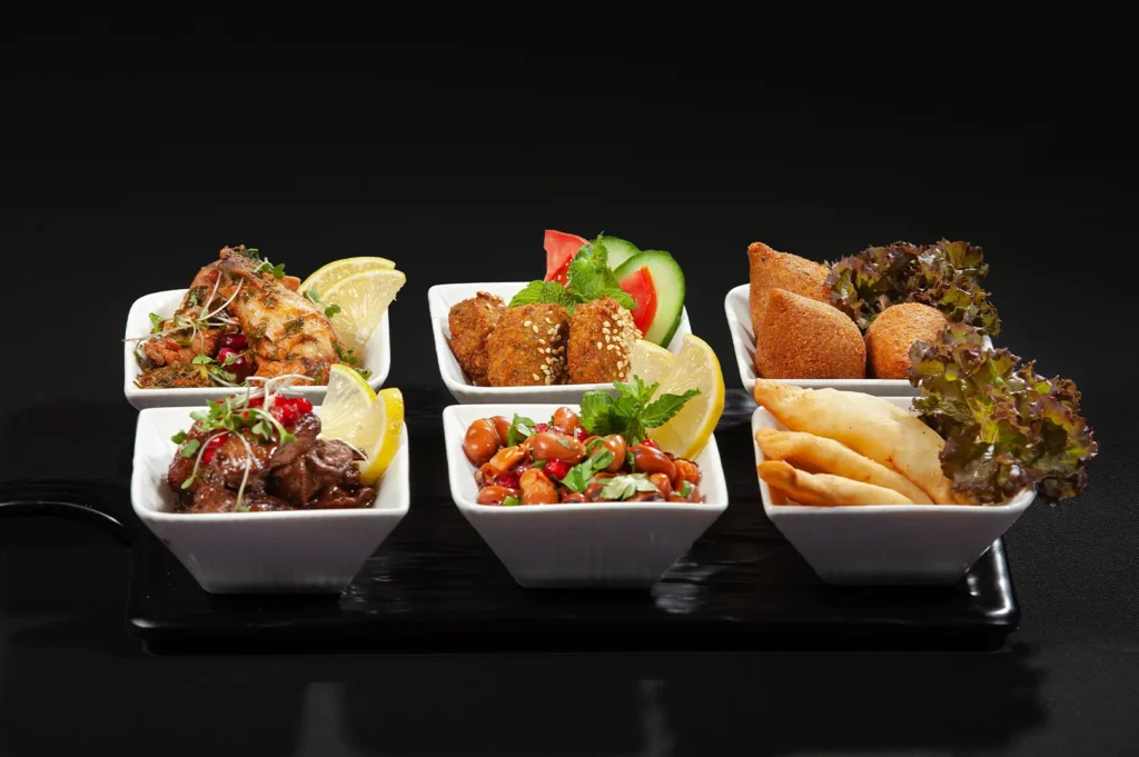 Dark-themed commercial food photography showcasing assorted appetizers and dishes in white bowls on a black tray.