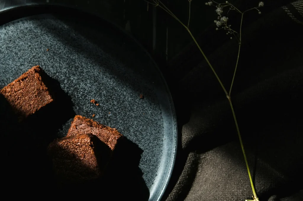 Dark moody food photography of chocolate brownies served on a black ceramic plate with minimalist dark styling.