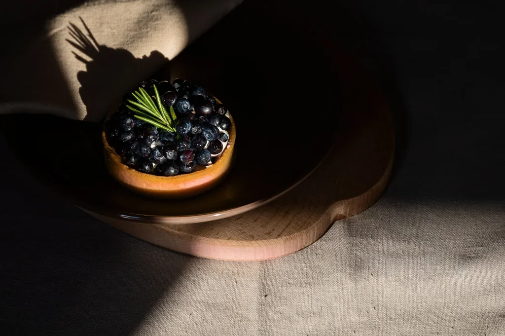 Dark moody food photography of a blueberry tart topped with fresh rosemary on a dark plate.