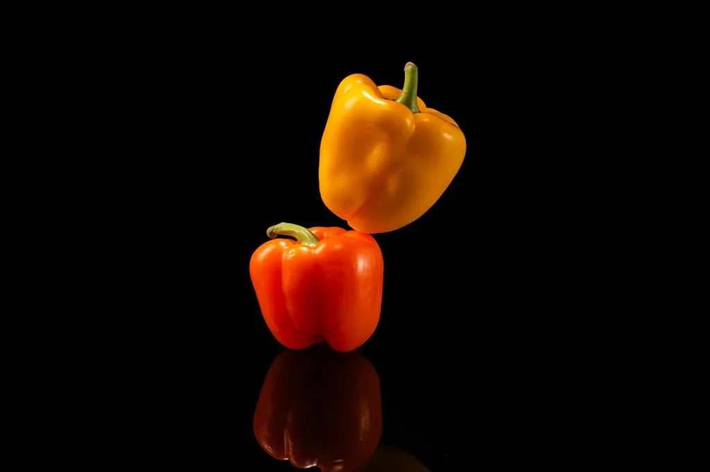 Professional dark background food photography of yellow and orange bell peppers with studio reflection.