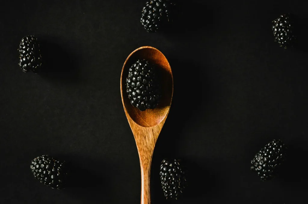 Fresh blackberries on dark background with a wooden spoon.