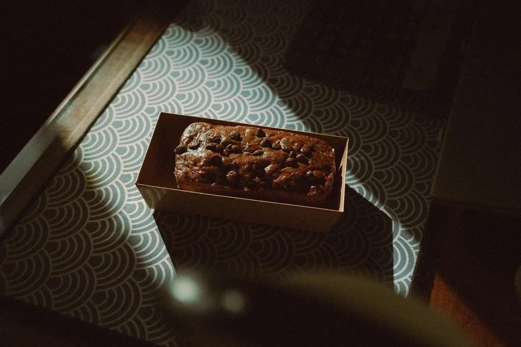 Chocolate banana bread inside brown paper packaging on a dark background.
