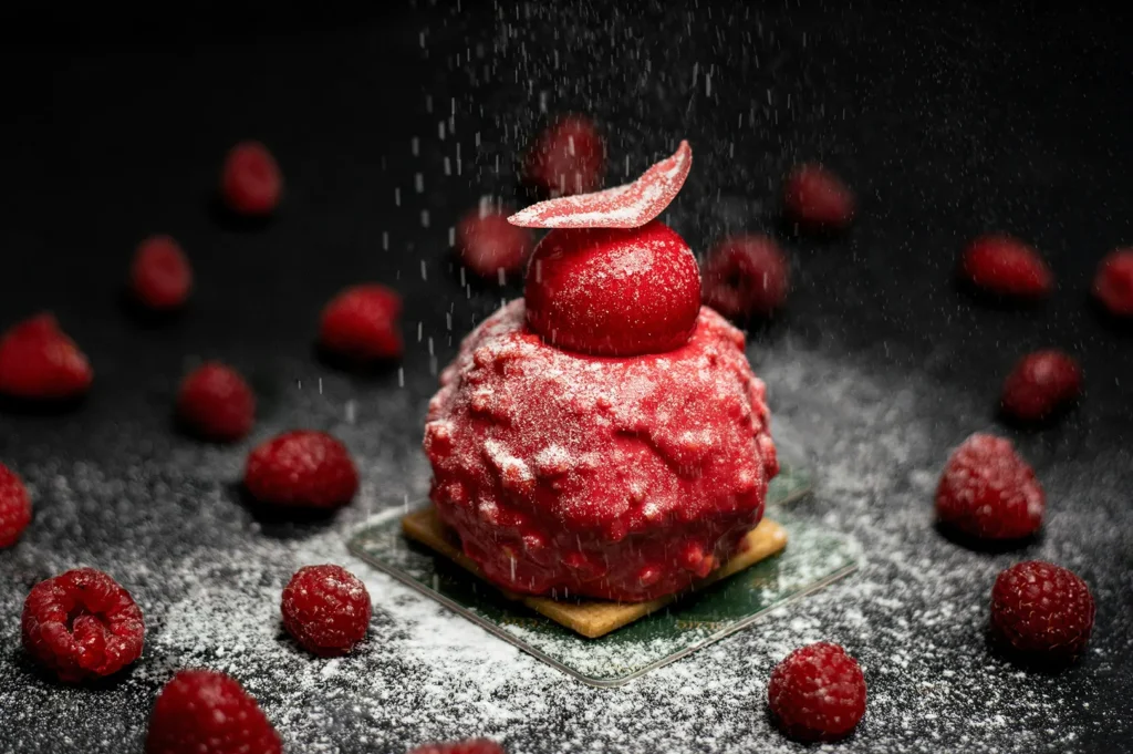 Red dessert pastry garnished with raspberries and powdered sugar on a dark background.