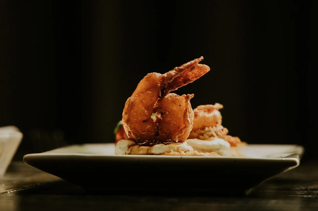 Crispy fried shrimp dish served on a plate with moody side lighting against a dark background.