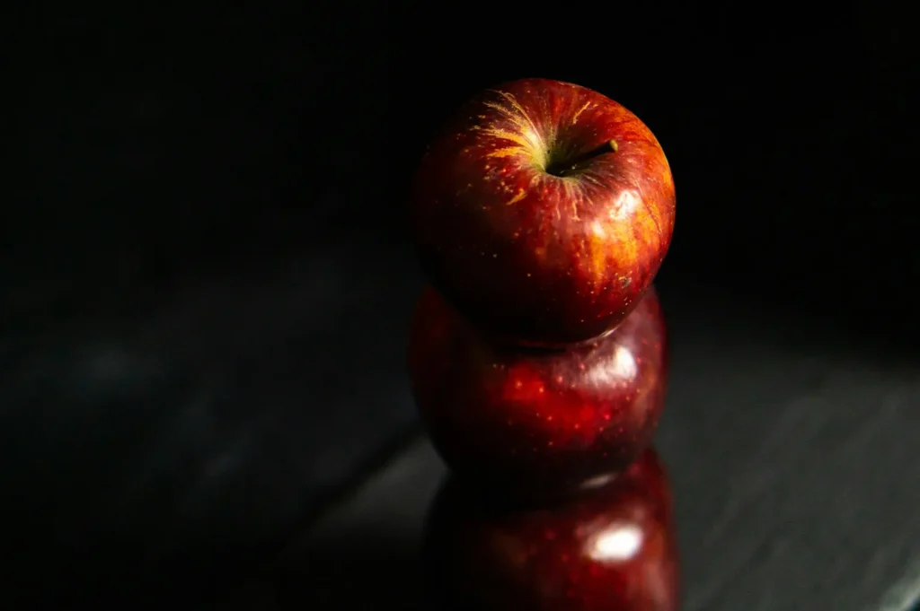 Three red apples stacked vertically on a dark surface with a moody black background.