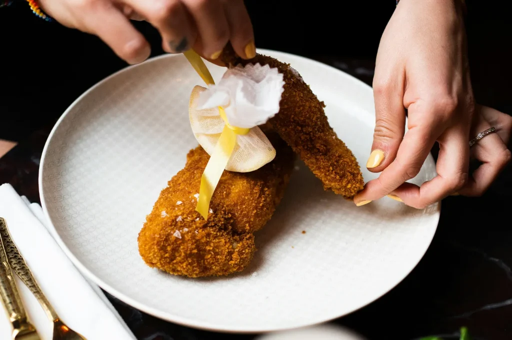 Chef plating a signature breaded fried chicken dish with a decorative ribbon on a white plate.