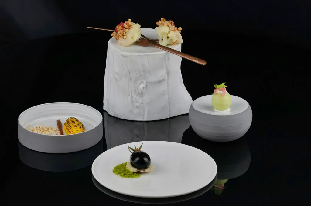 Dark moody food photography of gourmet dishes and white plating on a black reflective surface, illustrating RAW file processing.