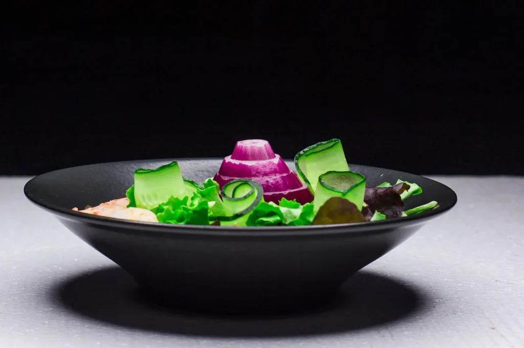 Dark mood food photography of a fresh vegetable salad in a black bowl against a black background.