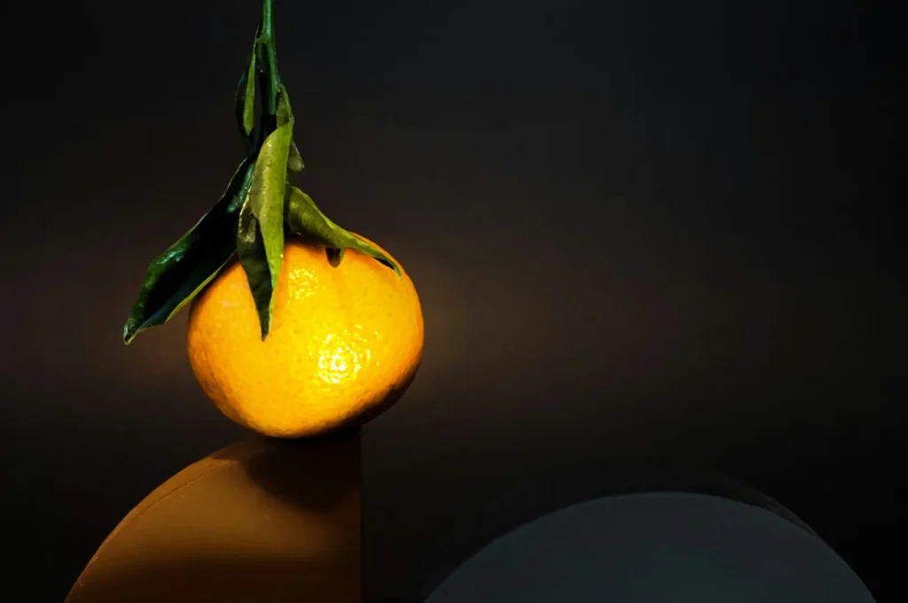 Low-key dark moody photography of a fresh mandarin orange with green leaves styled for restaurant social media marketing.