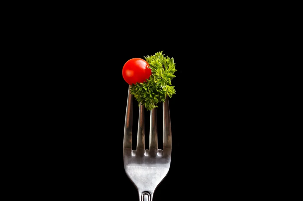 Professional food photography of a cherry tomato and parsley on a fork against a dark background for restaurant PR agencies.