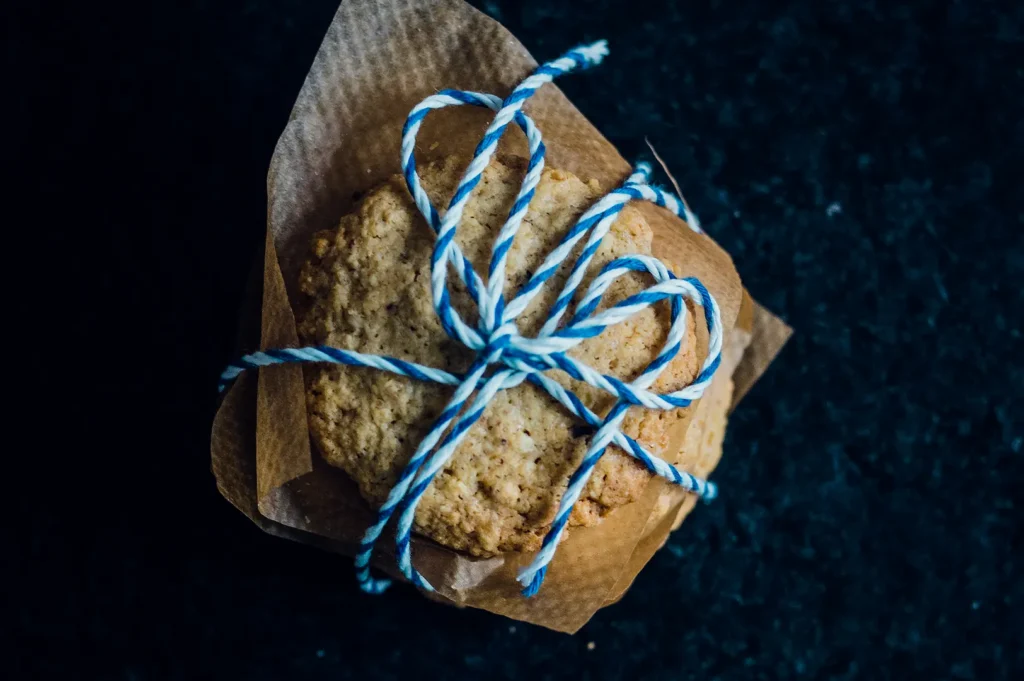 Handmade cookies wrapped in brown paper and blue string on a dark background.