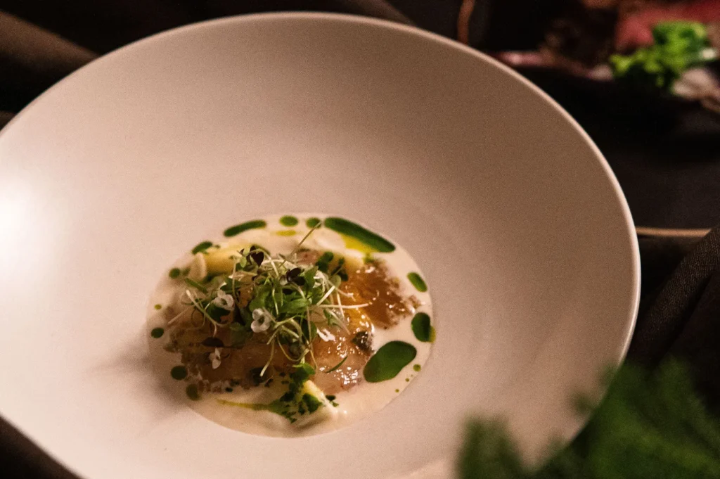 Fine dining dish served in a deep white bowl with green herb oil garnish.