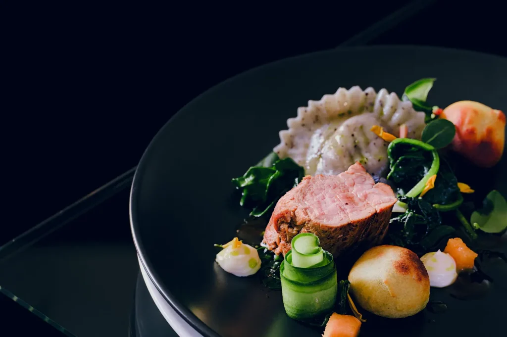 Gourmet pork dish with vegetables served on a black plate.
