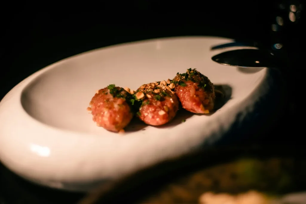 Dark moody food photography of three seasoned meat dishes garnished with herbs and nuts on a white oval plate.