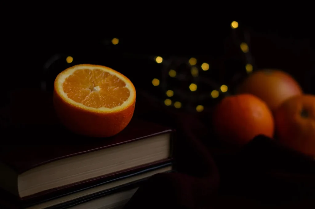 Fresh halved orange placed on top of stacked books in a dark moody setting with bokeh lights.