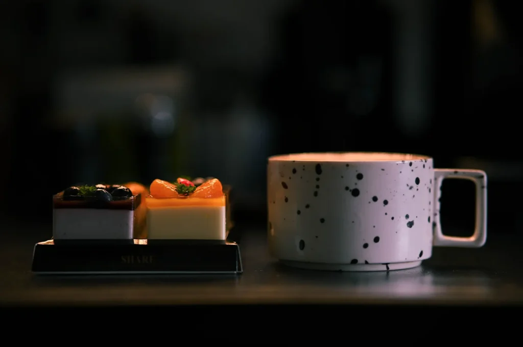 Moody food photography of small fruit cakes and a speckled coffee cup on a dark table for restaurant marketing guidelines.