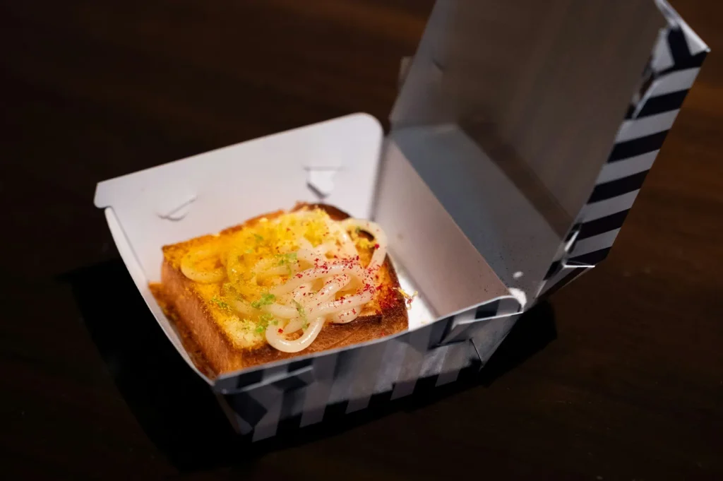 Gourmet takeaway food styling featuring toast in a branded takeout box on a dark background.
