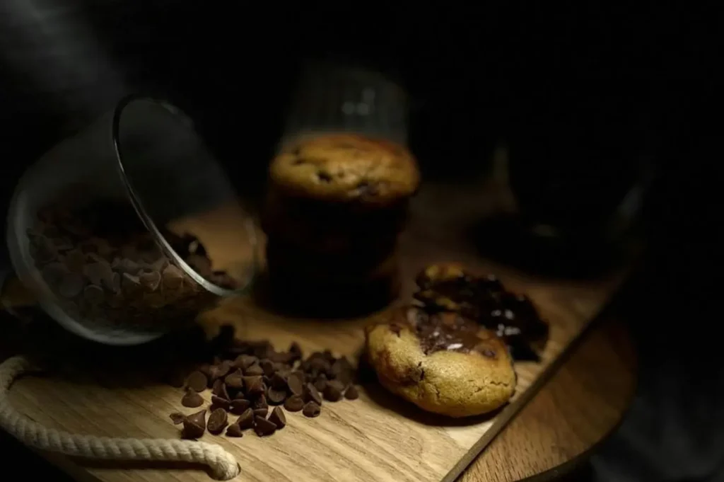 Dark moody food photography of chocolate chip cookies and chips on a wooden board.