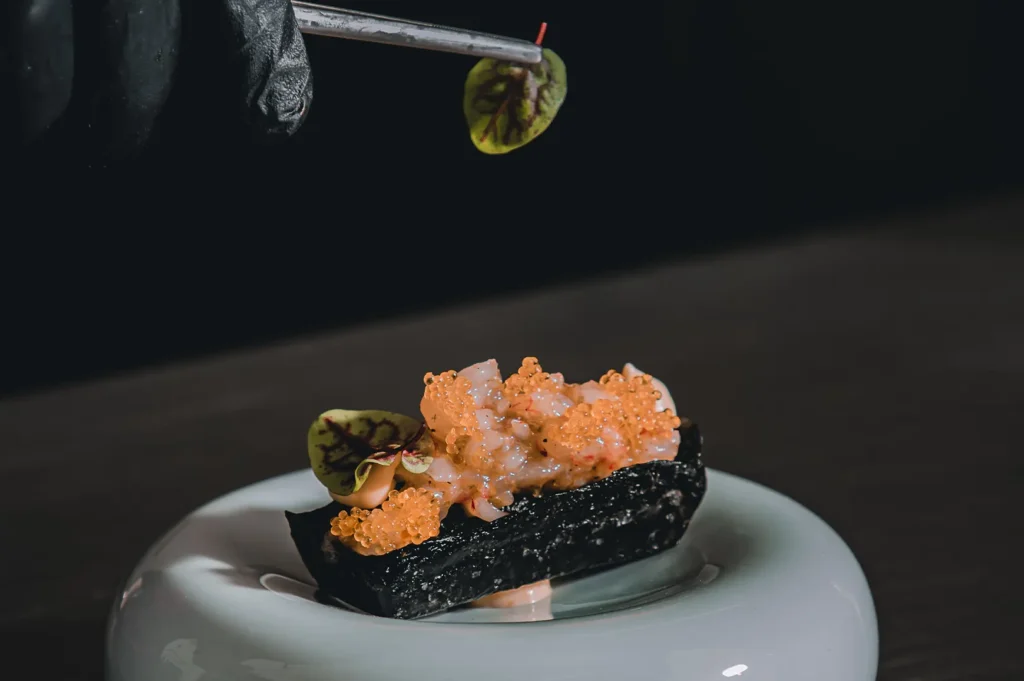 Chef using tweezers to garnish a dark gourmet dish with precision.