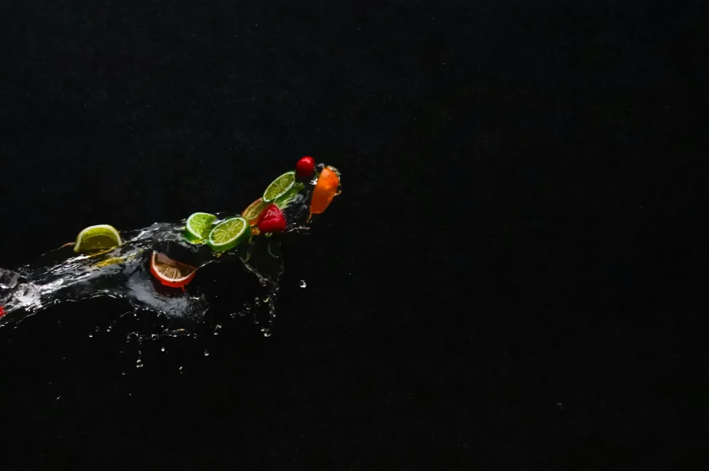 Dark mood food photography of fruit slices and water splash on black background showing fine translucent details.