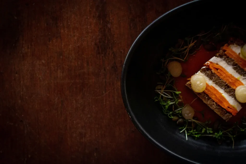 Dark moody food photography of a layered gourmet dish in a black bowl on a rustic wooden table.