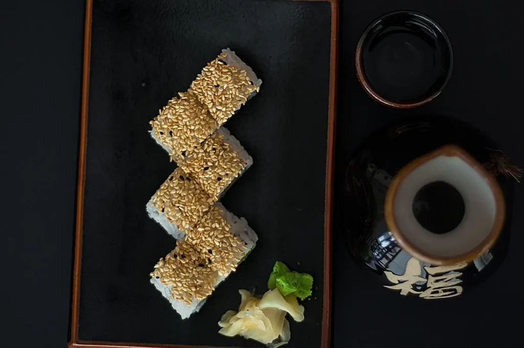Top-down view of a dark moody sushi set served on a black plate with wasabi and soy sauce.