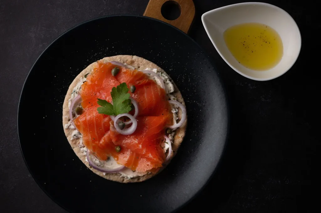 Smoked salmon flatbread with cream cheese and red onion on a black plate.