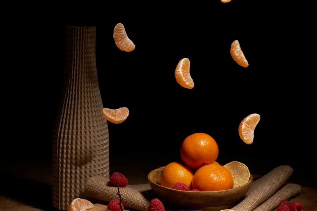 Dramatic dark food photography with falling orange slices and a bowl of fresh mandarins.